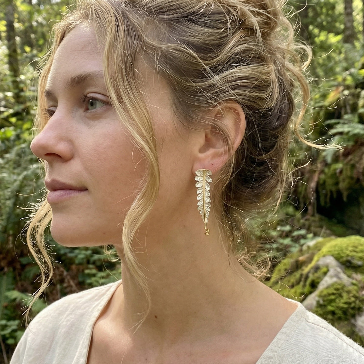 Woman with styled hair and earrings in a forest setting