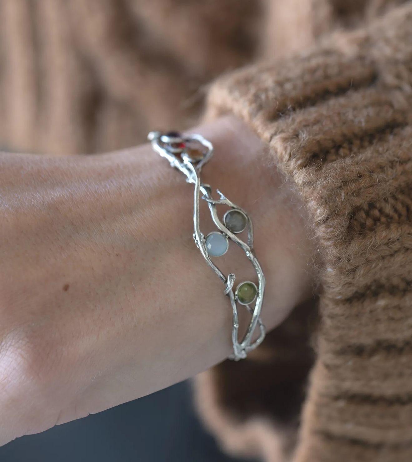 Drift Bracelet, a nature-inspired, hand-crafted sterling silver design featuring gemstone accents in soft earthy tones, styled with a cozy sweater.