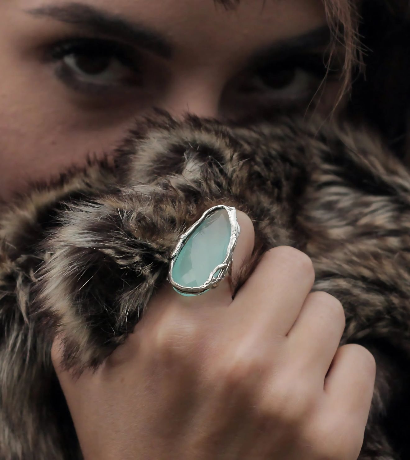 Close-up of the Karma Ring, a hand-crafted sterling silver design featuring a soft aqua chalcedony gemstone, worn with an elegant fur texture background
