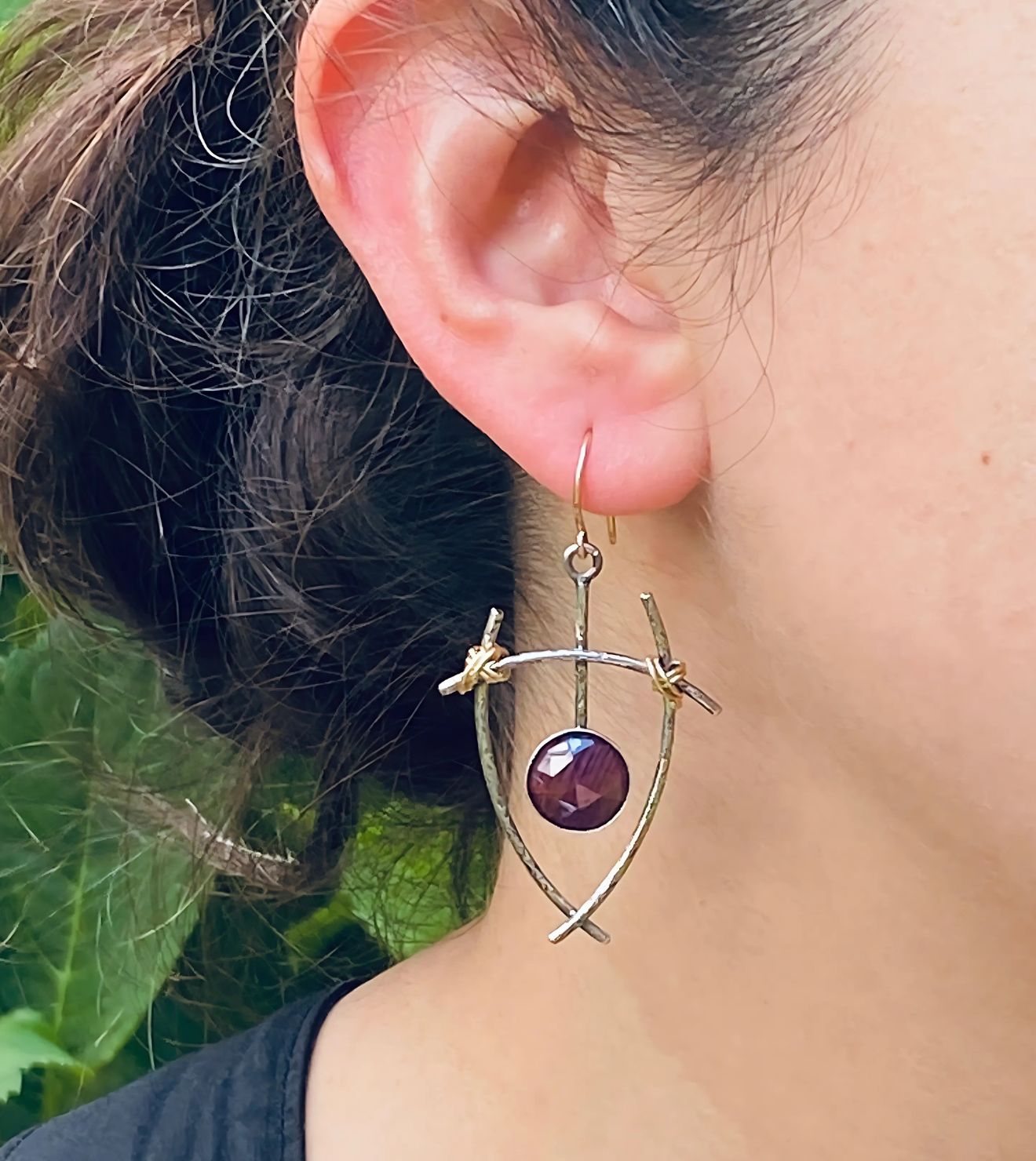 Twilight Earrings featuring hand-crafted sterling silver and a deep purple gemstone, accented with intricate branch-inspired details, worn in an outdoor setting.