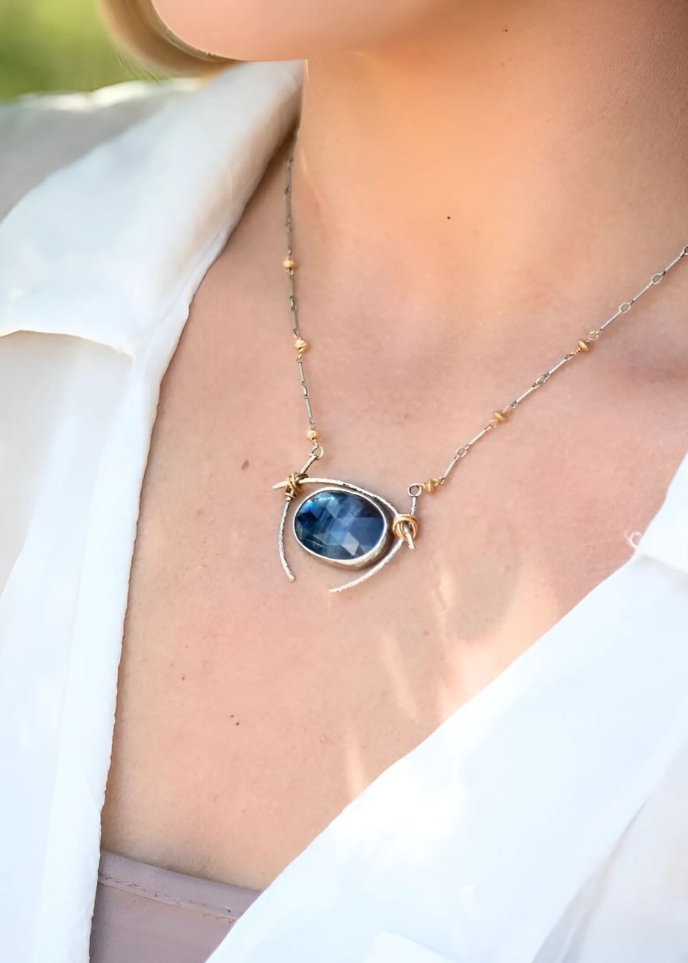 Close-up of a model showcasing the Dream Collection, wearing a nature-inspired, hand-crafted sterling silver necklace with a bold blue gemstone centerpiece and gold accents.